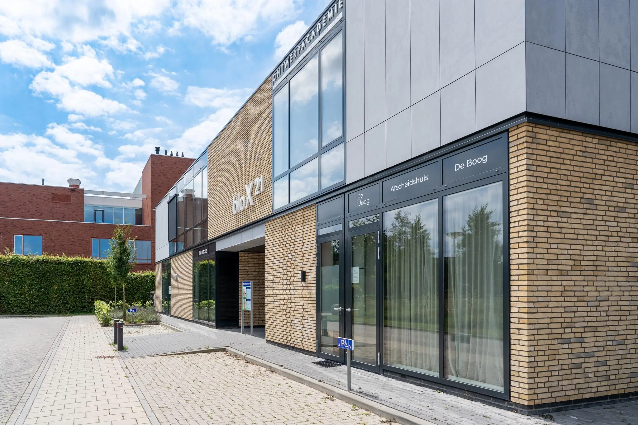 Moderne gevel van het gebouw HoX21 met het afscheids­huis De Boog aan de Handboog.