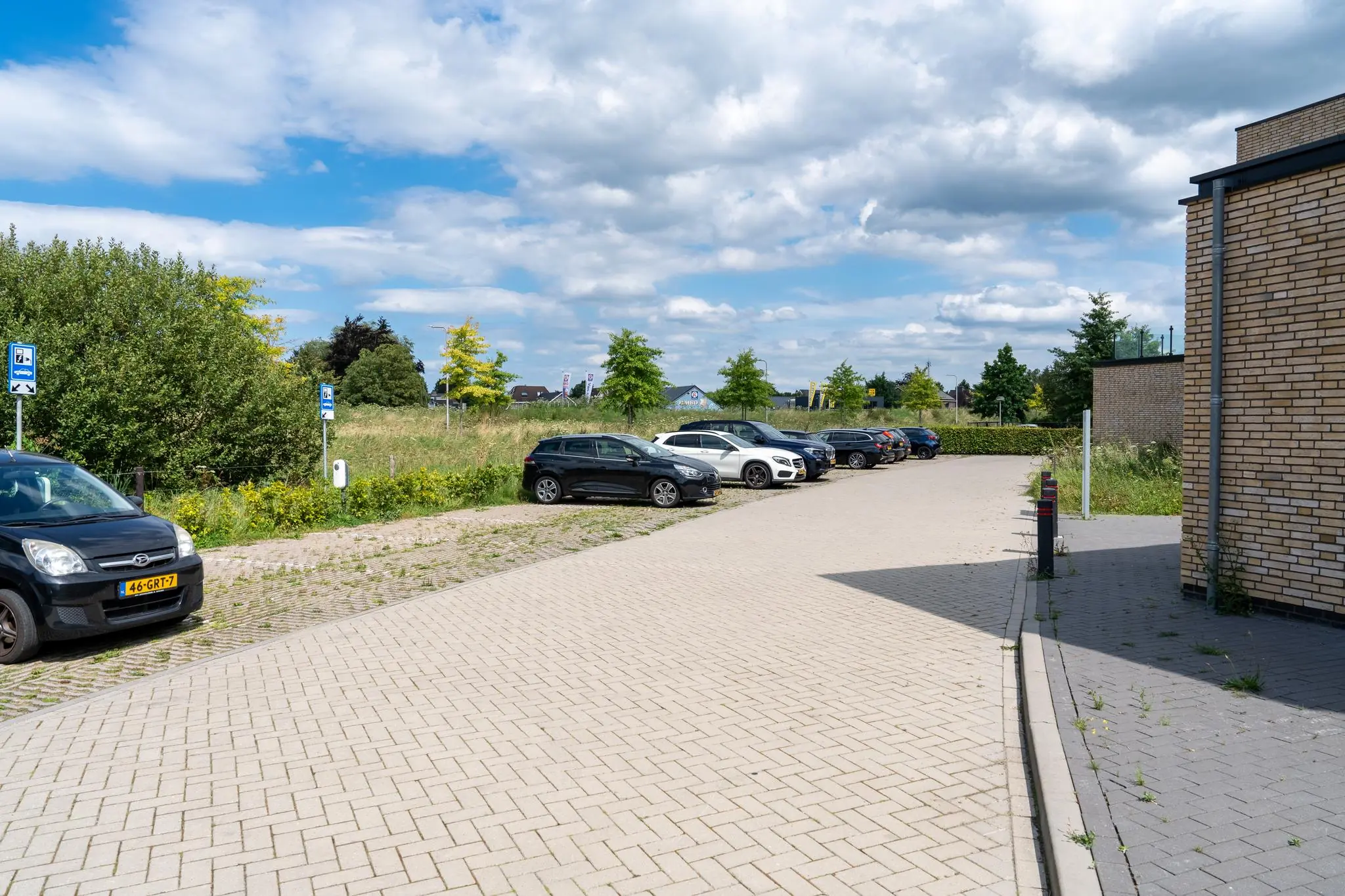 Parkeerplaats bij een gebouw aan de Handboog met auto's en naastgelegen groenstrook op een zonnige dag.
