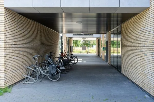 Overdekte doorgang tussen twee gebouwen met geparkeerde fietsen tegen een bakstenen muur.