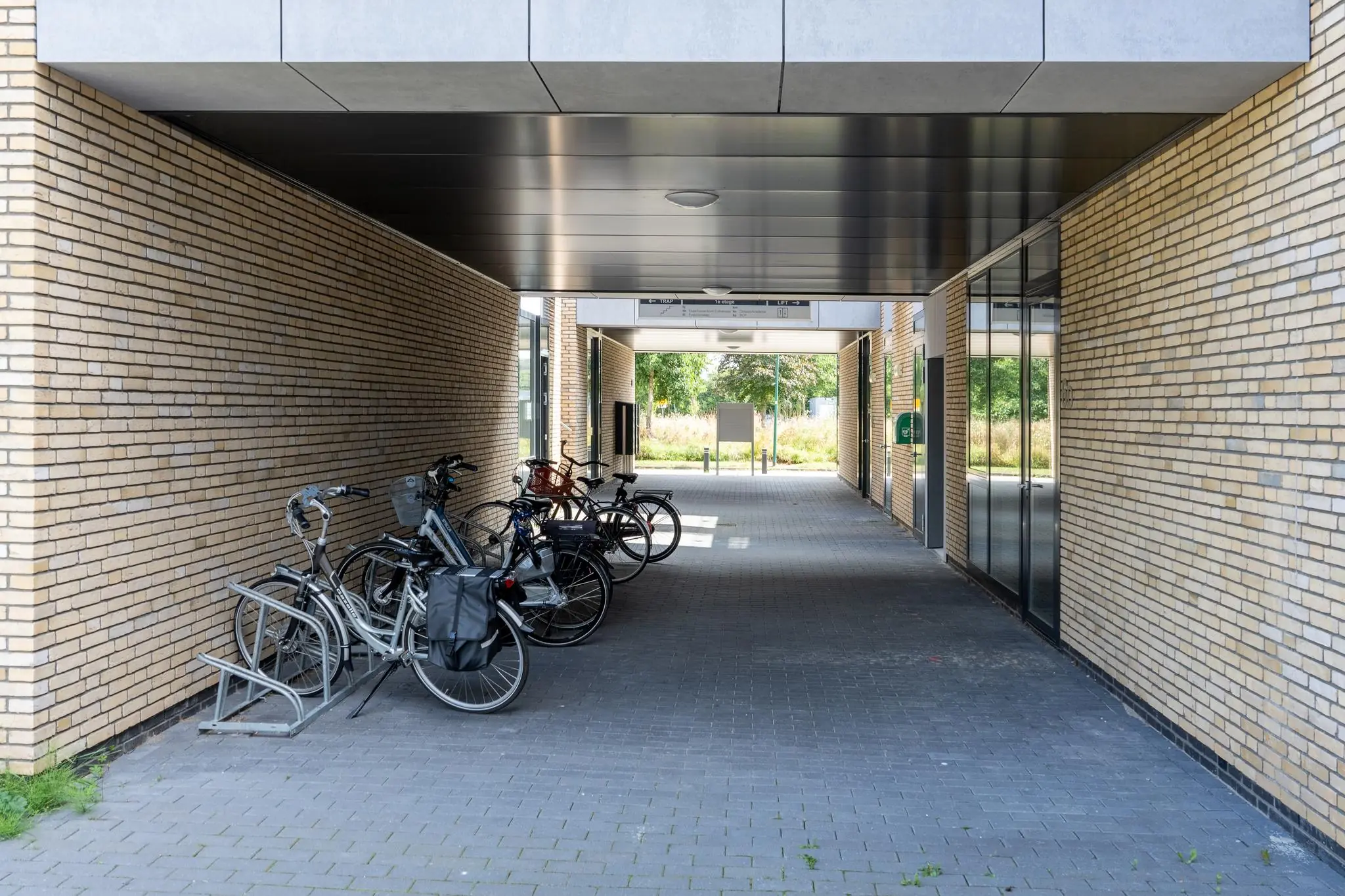 Overdekte doorgang tussen twee gebouwen met geparkeerde fietsen tegen een bakstenen muur.