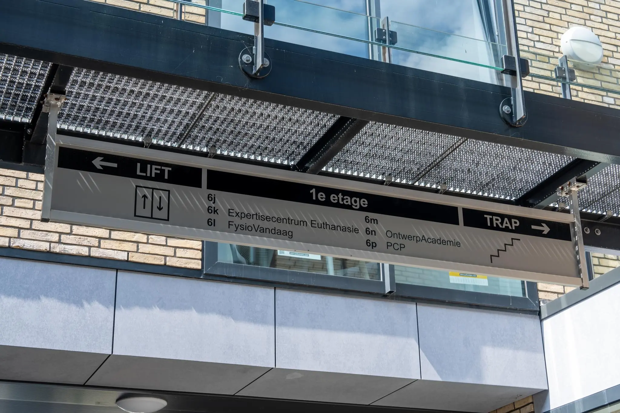 Wegwijzer op een gebouw met aanduidingen voor lift en trap naar de eerste etage met onder andere het Expertisecentrum Euthanasie en de OntwerpAcademie.