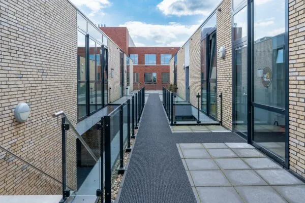 Moderne, verhoogde galerij tussen bakstenen woongebouwen met glazen balustrades in wooncomplex Handboog.