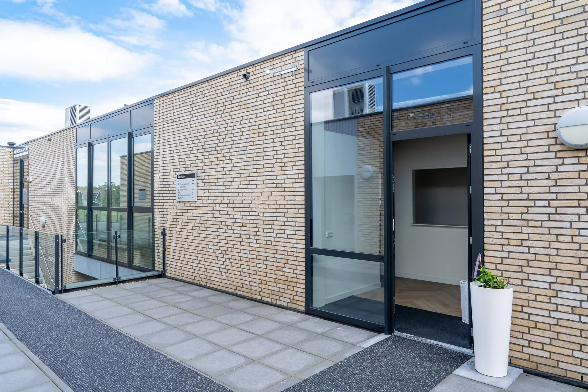 Ingang van een modern gebouw aan de Handboog met een open glazen deur en een bakstenen gevel.