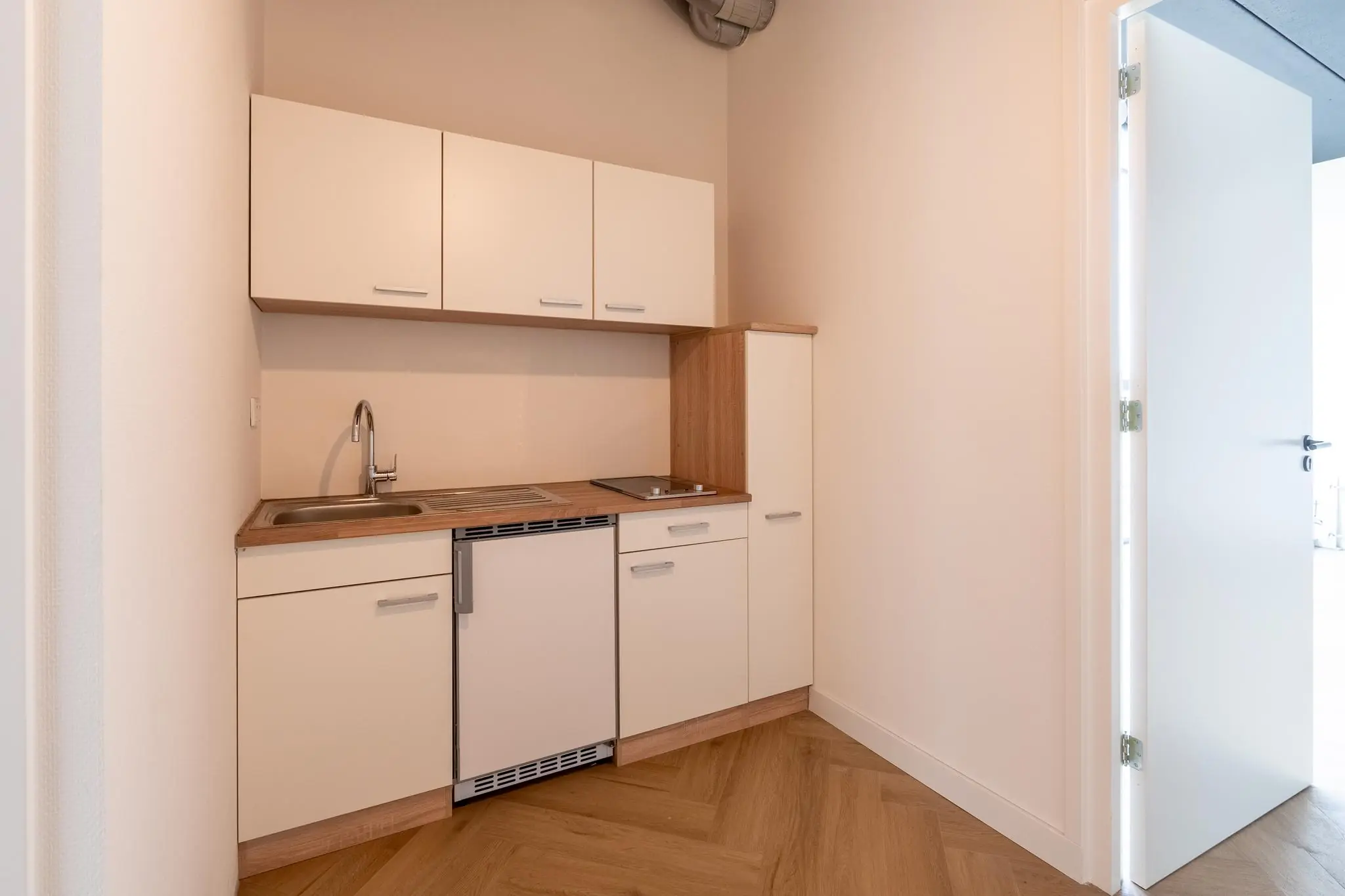 Compacte kitchenette met witte kastjes, houten werkblad en een spoelbak in een lichte ruimte.