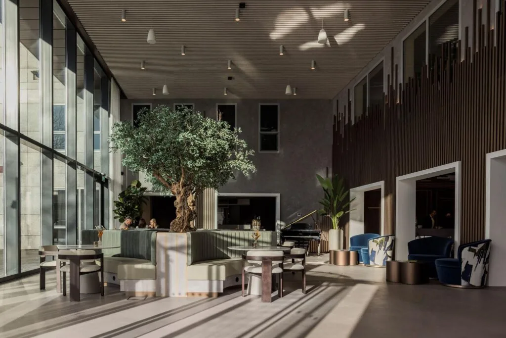 Moderne, lichte lounge met grote raampartijen, een centrale boom en stijlvolle zitplekken in het Diemerhof gebouw.