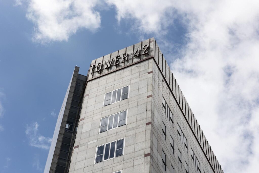 Hoekaanzicht van de bovenste verdiepingen van kantoorgebouw Tower 42 in Diemen tegen een deels bewolkte lucht.