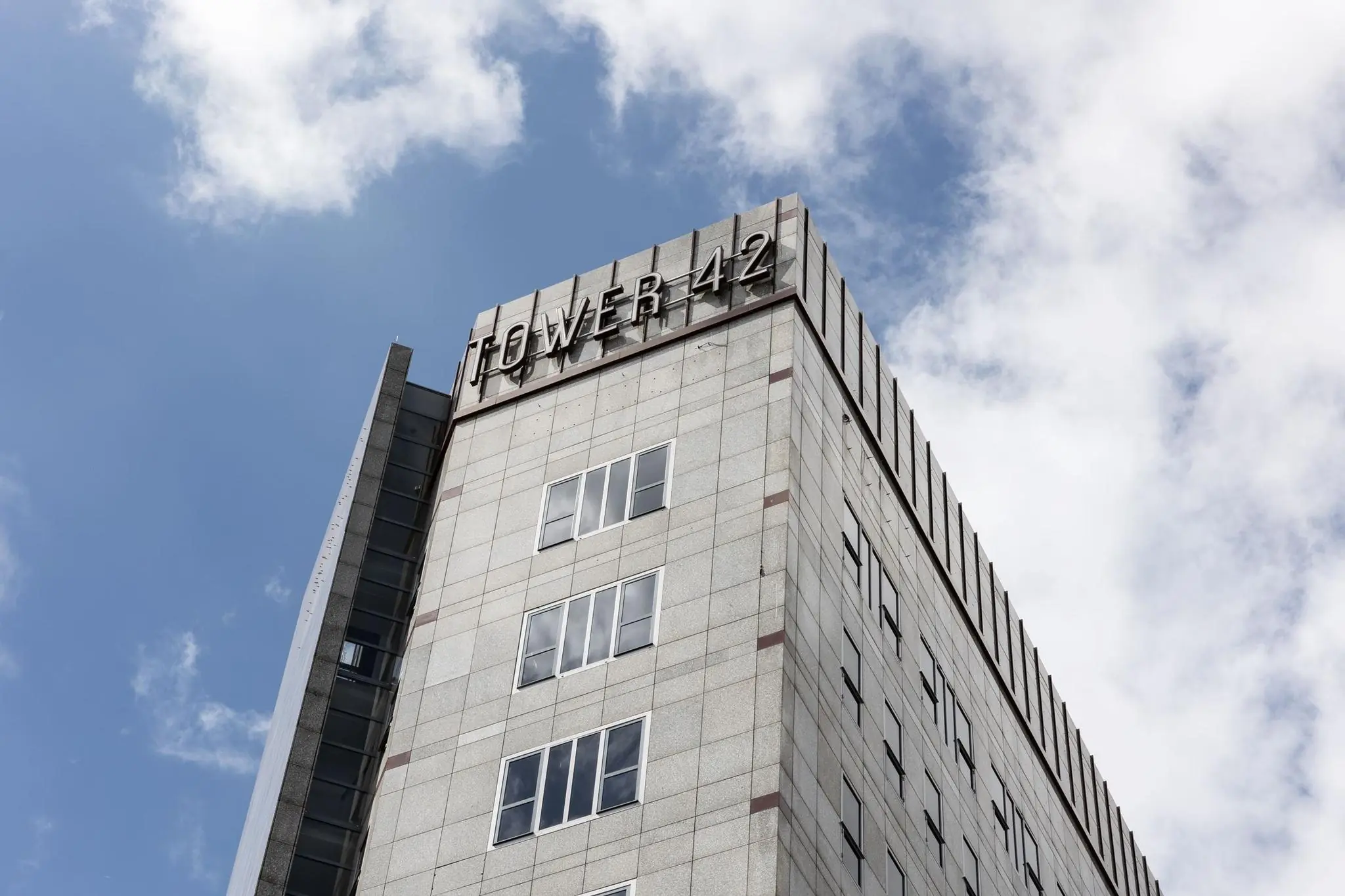 Hoekaanzicht van de bovenste verdiepingen van kantoorgebouw Tower 42 in Diemen tegen een deels bewolkte lucht.