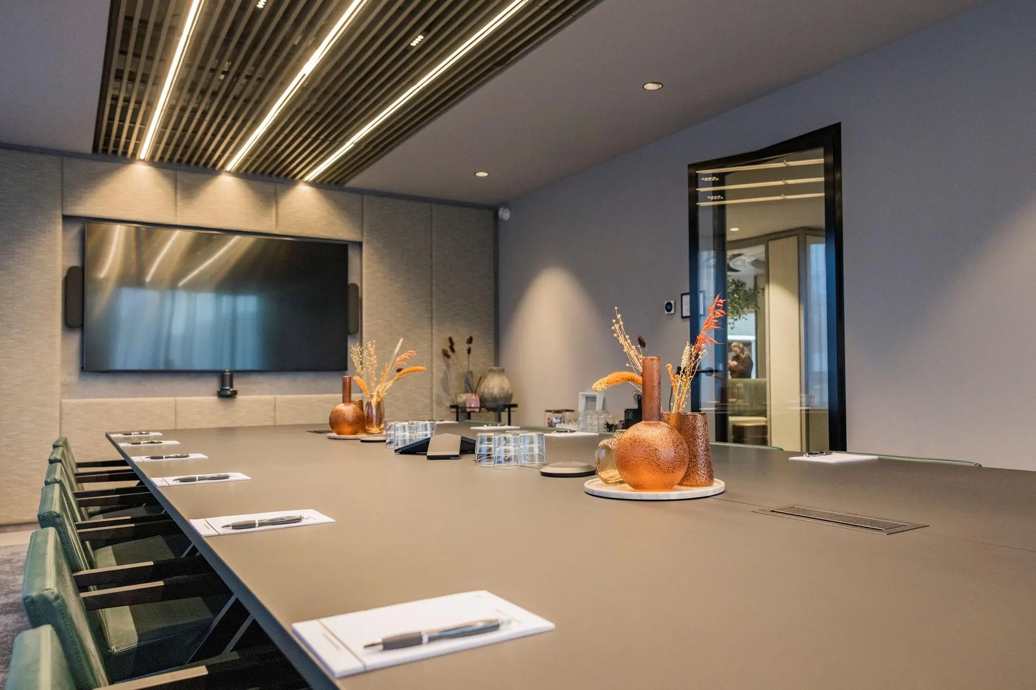 Moderne vergaderruimte in Diemerhof met een lange tafel, notitieblokken, een groot scherm en decoratieve vazen.