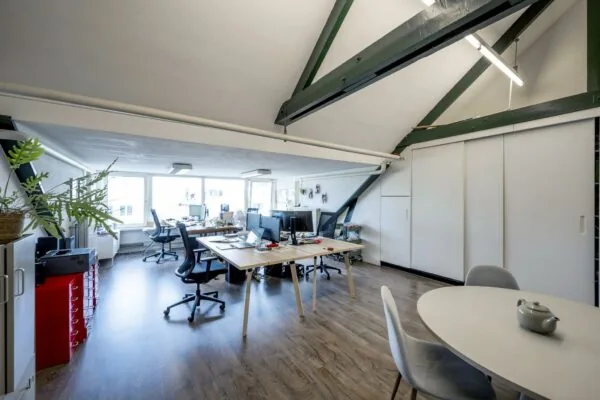 Moderne kantoorruimte aan het WG-plein met schuin dak, houten vloer, meerdere werkplekken en een ronde vergadertafel.