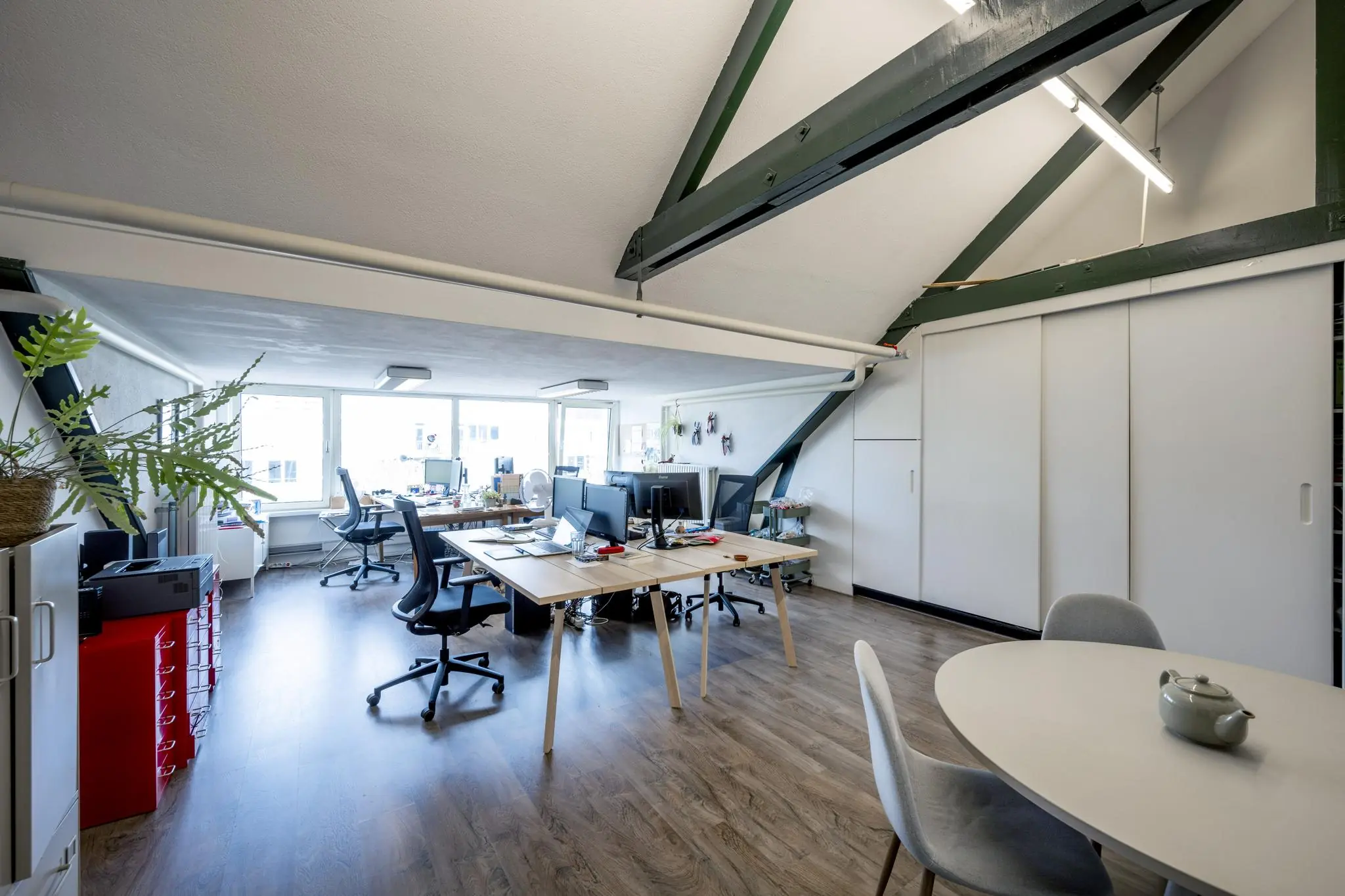 Moderne kantoorruimte aan het WG-plein met schuin dak, houten vloer, meerdere werkplekken en een ronde vergadertafel.