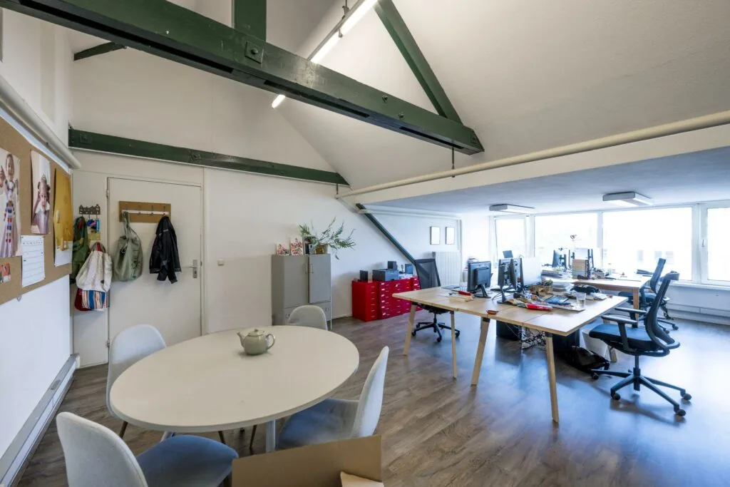 Ruim en licht kantoor op het WG-plein met houten vloer, werkplekken, een ronde vergadertafel en zichtbare houten balken.