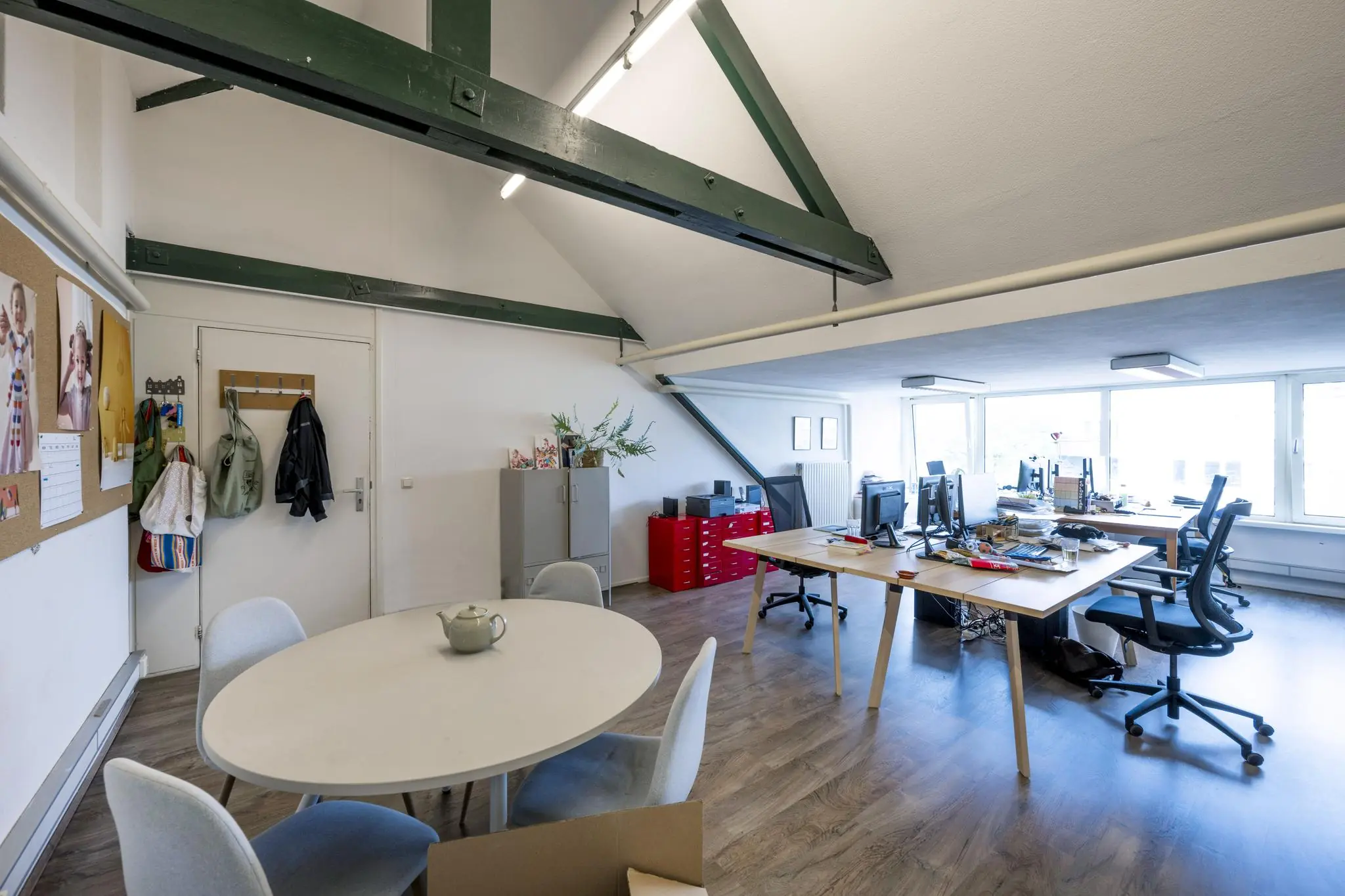 Ruim en licht kantoor op het WG-plein met houten vloer, werkplekken, een ronde vergadertafel en zichtbare houten balken.