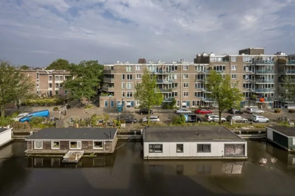 Woonboten aan een gracht met op de achtergrond appartementen aan het WG-plein in Amsterdam.