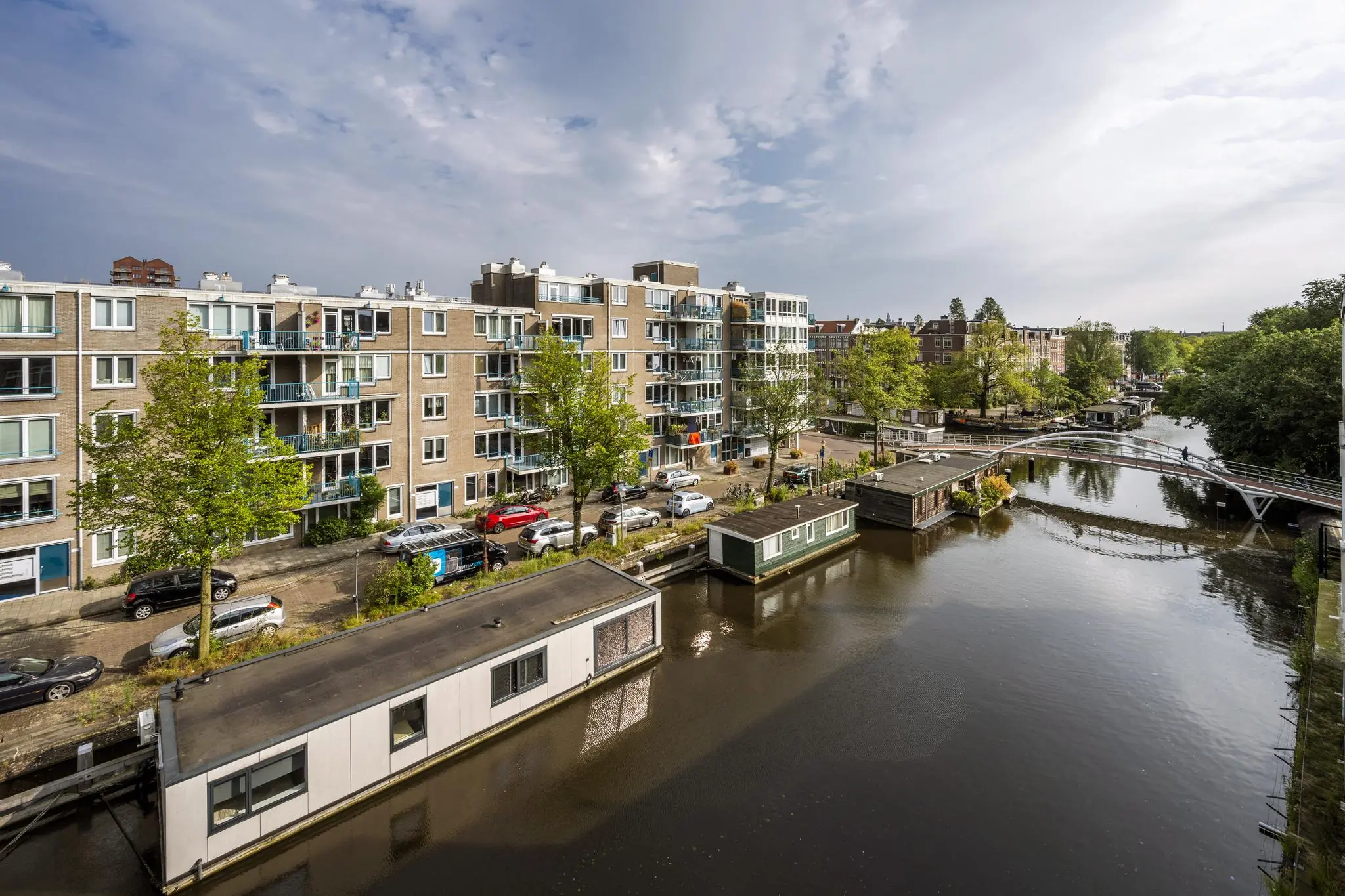 Uitzicht op het WG-Plein in Amsterdam met woonboten in de gracht, een voetgangersbrug en omliggende appartementen.