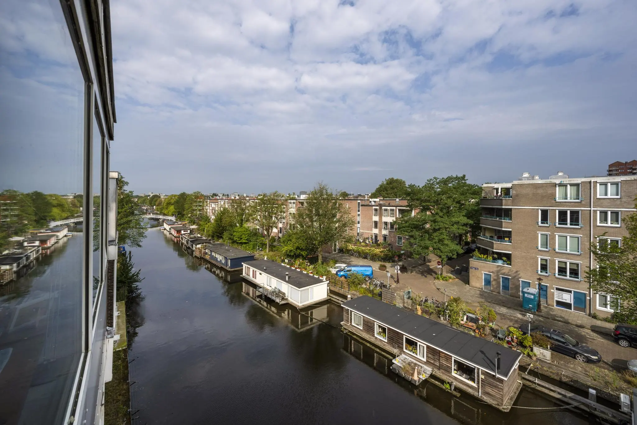 Uitzicht vanaf een gebouw op het WG-plein in Amsterdam met woonboten in het kanaal en omliggende woonhuizen.