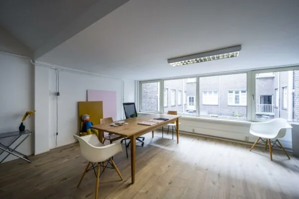 Licht en modern kantoor aan het WG-plein met houten vloer, grote ramen en een vergadertafel.