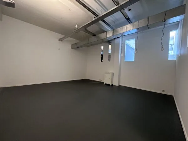 Lege, industriële ruimte aan de Pilotenstraat met witte muren, zwart vloer en zichtbare luchtkanalen aan het plafond.