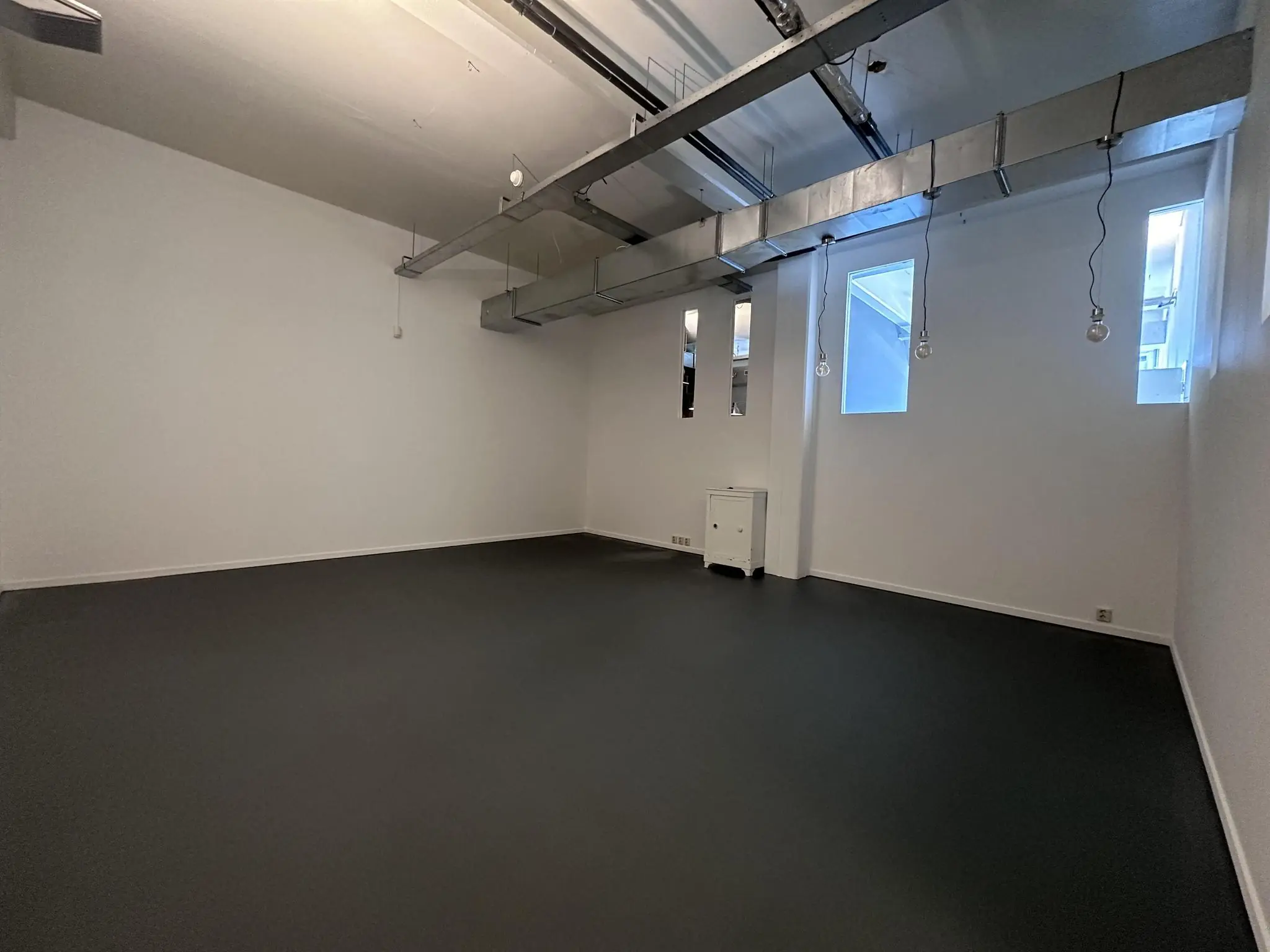Lege, industriële ruimte aan de Pilotenstraat met witte muren, zwart vloer en zichtbare luchtkanalen aan het plafond.