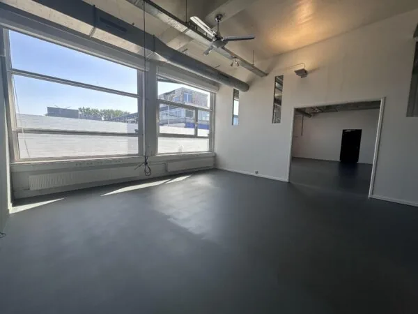 Lichte, lege kantoorruimte aan de Pilotenstraat met grote ramen, grijze vloer en industriële plafonddetails.