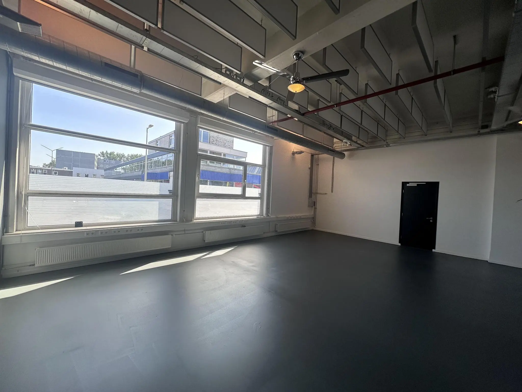 Lichte, lege kantoorruimte aan de Pilotenstraat met grote ramen en industrieel plafond.