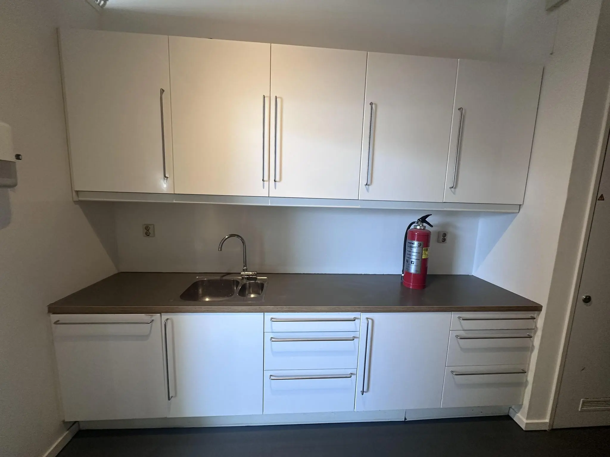 Keukenblok met witte kasten, een gootsteen en een brandblusser op het aanrecht in een ruimte aan de Pilotenstraat.