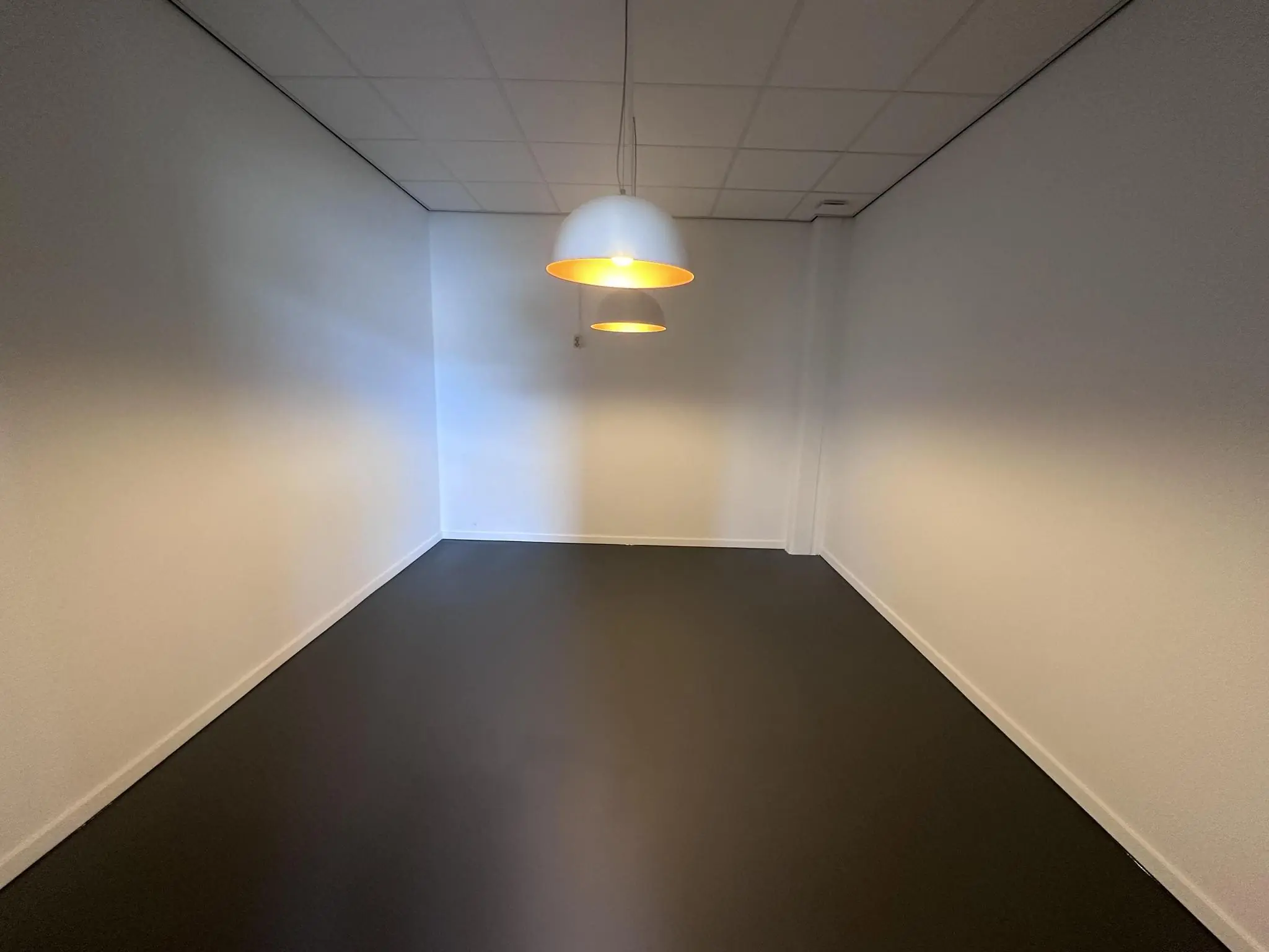 Lege kantoorruimte aan de Pilotenstraat met witte muren, donkere vloer en twee hanglampen aan het plafond.