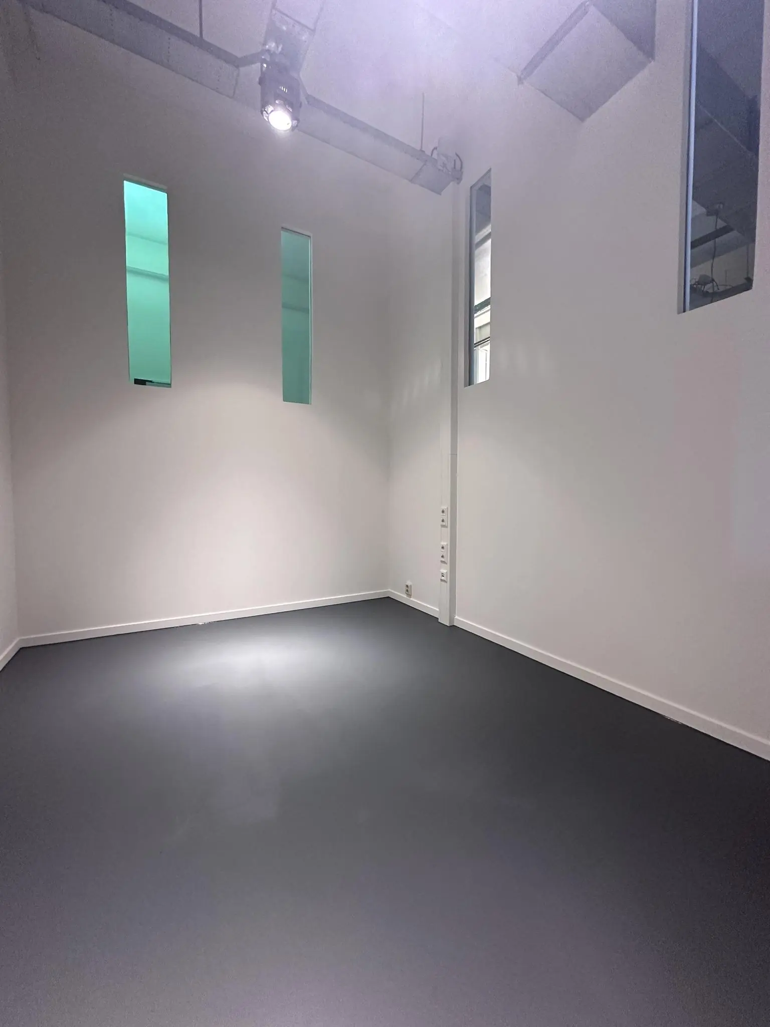 Leeg, witgeschilderd vertrek met donkere vloer en hoge smalle ramen aan de Pilotenstraat.