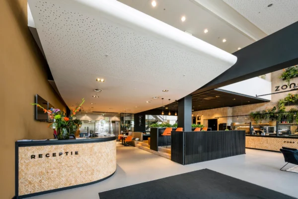 Receptie van een modern, stijlvol ingerichte lobby met bloemen op de balie en een zithoek op de achtergrond.