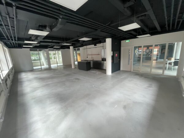 Lege, moderne kantoorruimte met betonnen vloer, zwarte plafonds en een keukenblok in het midden.