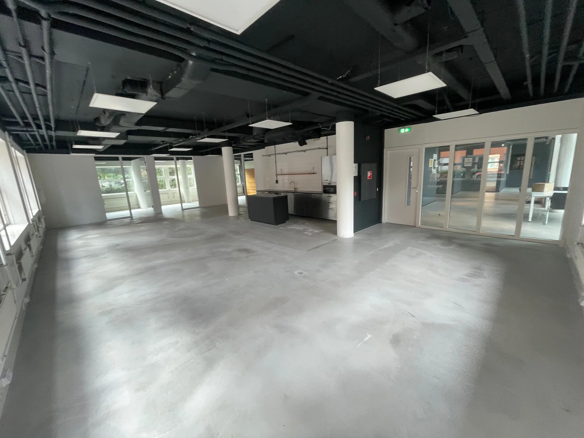 Lege, moderne kantoorruimte met betonnen vloer, zwarte plafonds en een keukenblok in het midden.