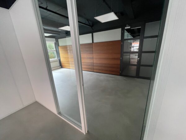 Moderne, lege kantoorruimte met betonnen vloer, glazen wanden en een houten wandpaneel.