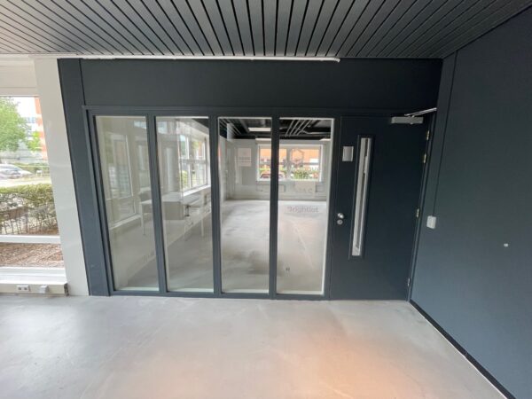 Glazen entree met zwarte kozijnen en deur van het kantoorpand Brightlot.