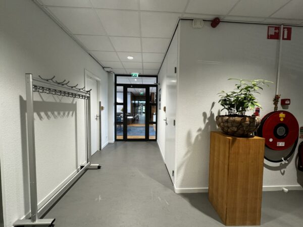 Hal met kapstok, plant in stenen bloempot op houten sokkel en brandslanghaspel in een kantoorgebouw aan de Softwareweg.