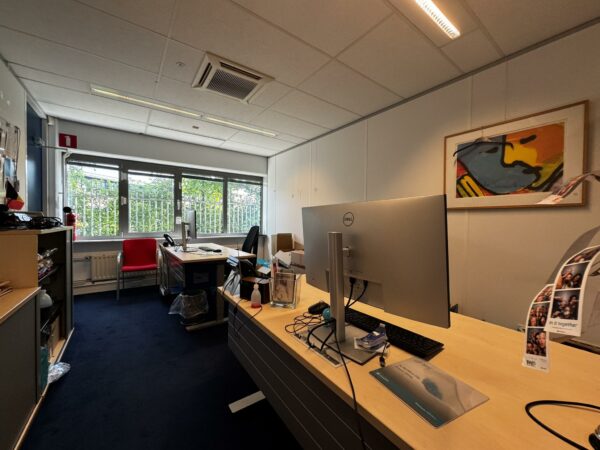 Modern kantoor met twee bureaus, computers en een groot raam met uitzicht op groen.
