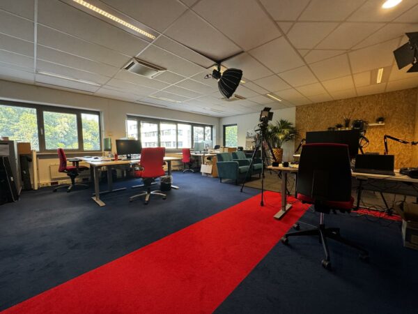 Moderne kantoorruimte aan de Softwareweg met bureaus, rode bureaustoelen, camera-apparatuur en studiolampen.