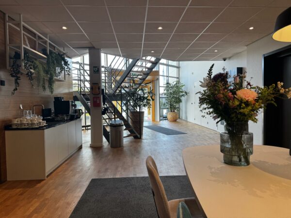Moderne kantoorentree aan de Softwareweg met een koffiecorner, trap naar boven en een vaas bloemen op de voorgrond.