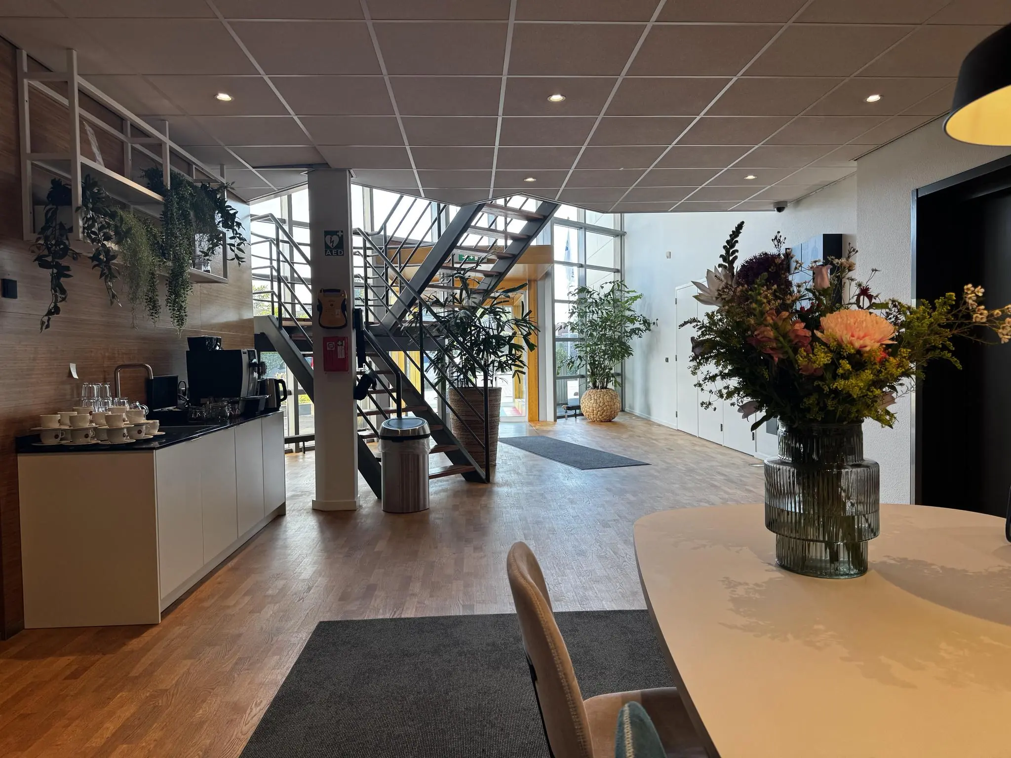 Moderne kantoorentree aan de Softwareweg met een koffiecorner, trap naar boven en een vaas bloemen op de voorgrond.