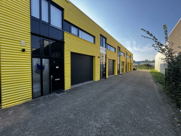 Rij met gele bedrijfsunits aan de Ambachtsweg met zwarte deuren en rolluiken.