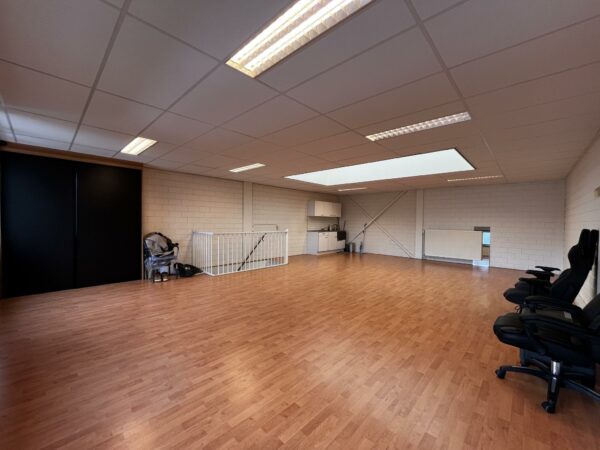 Ruime kantoorruimte aan de Ambachtsweg met houten vloer, systeemplafond, pantry en enkele bureaustoelen.