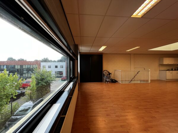 Ruim en licht kantoorinterieur aan de Ambachtsweg met houten vloer, grote ramen en uitzicht op een bedrijventerrein.
