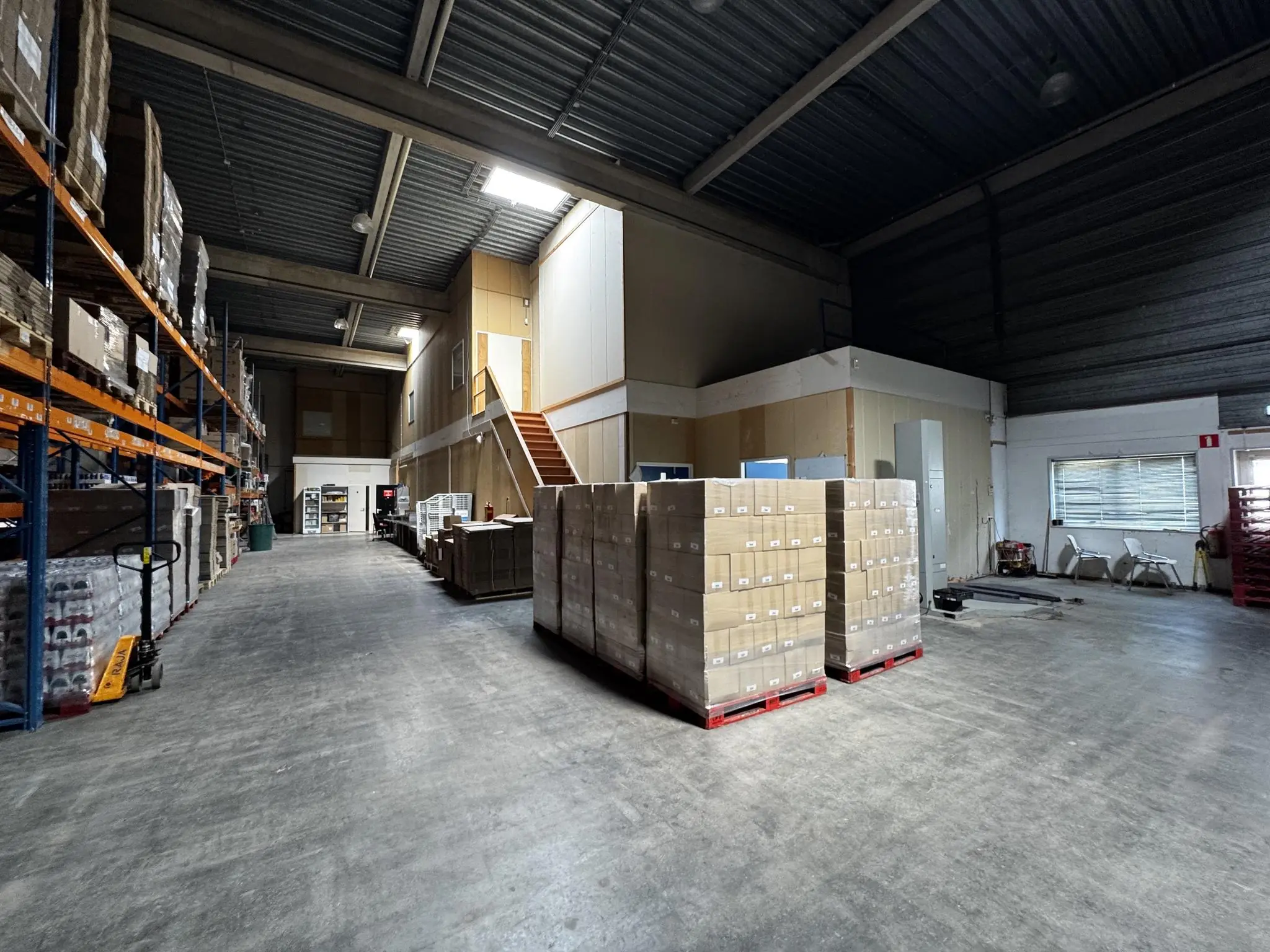 Ruime opslagloods aan de Lorentzweg met stellingen vol dozen en pallets met voorraad op de vloer.