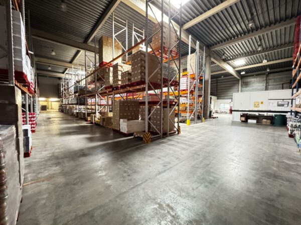 Magazijn aan de Lorentzweg met hoge stellingen vol dozen en brede looppaden.