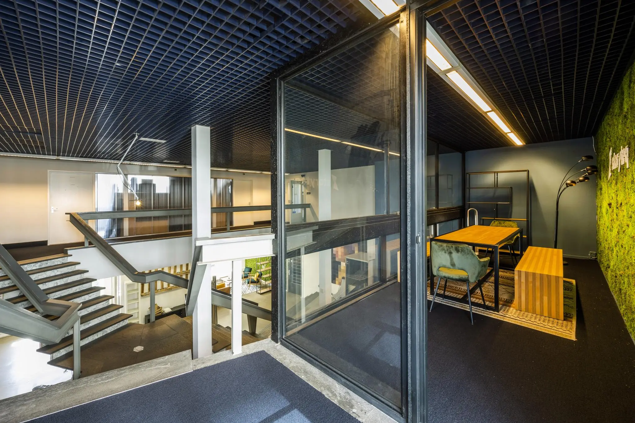 Modern kantoorinterieur aan de Vliegtuigstraat met open trappenhuis en glazen vergaderruimte met groene moswand.