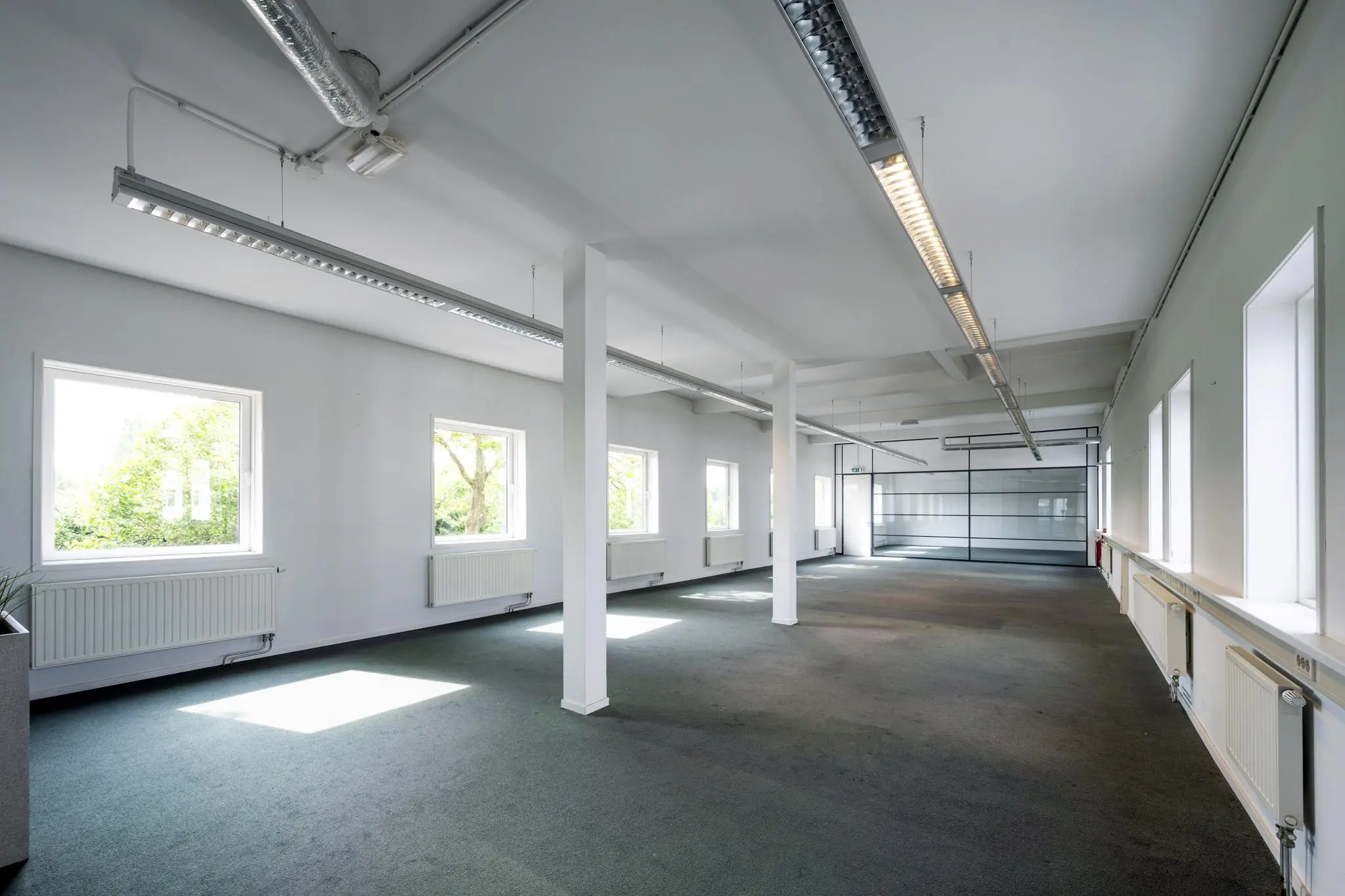 Lichte, lege kantoorruimte aan de Vliegtuigstraat met grote ramen en tapijtvloer.