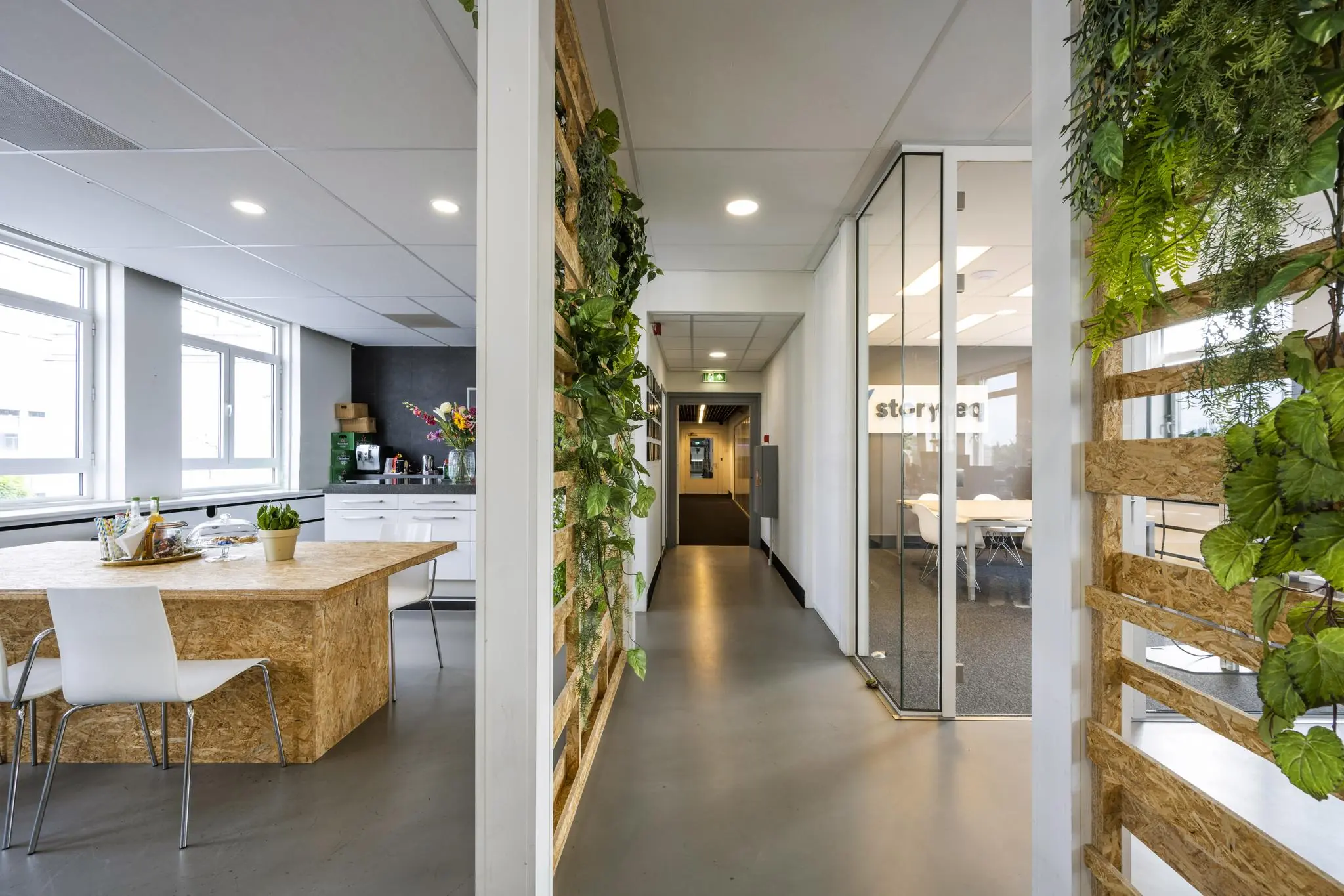 Modern kantoorinterieur aan de Vliegtuigstraat met een open keuken, vergaderruimte en groene wanddecoratie.