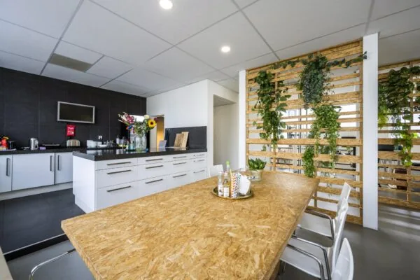 Moderne kantoorkeuken aan de Vliegtuigstraat met houten tafel, witte kasten en groene plantenwand.
