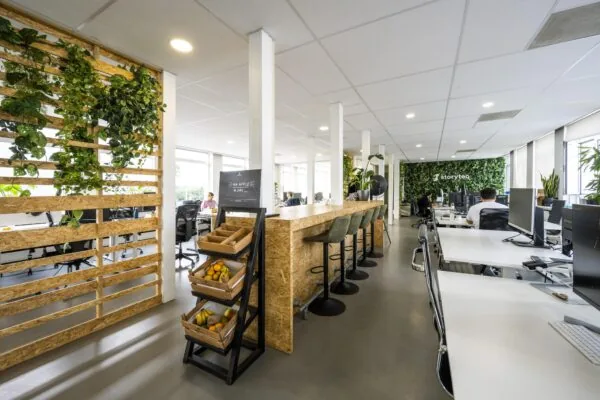 Modern kantoorinterieur aan de Vliegtuigstraat met open werkplekken, een hoge tafel met barkrukken, veel groen en een fruitrek.