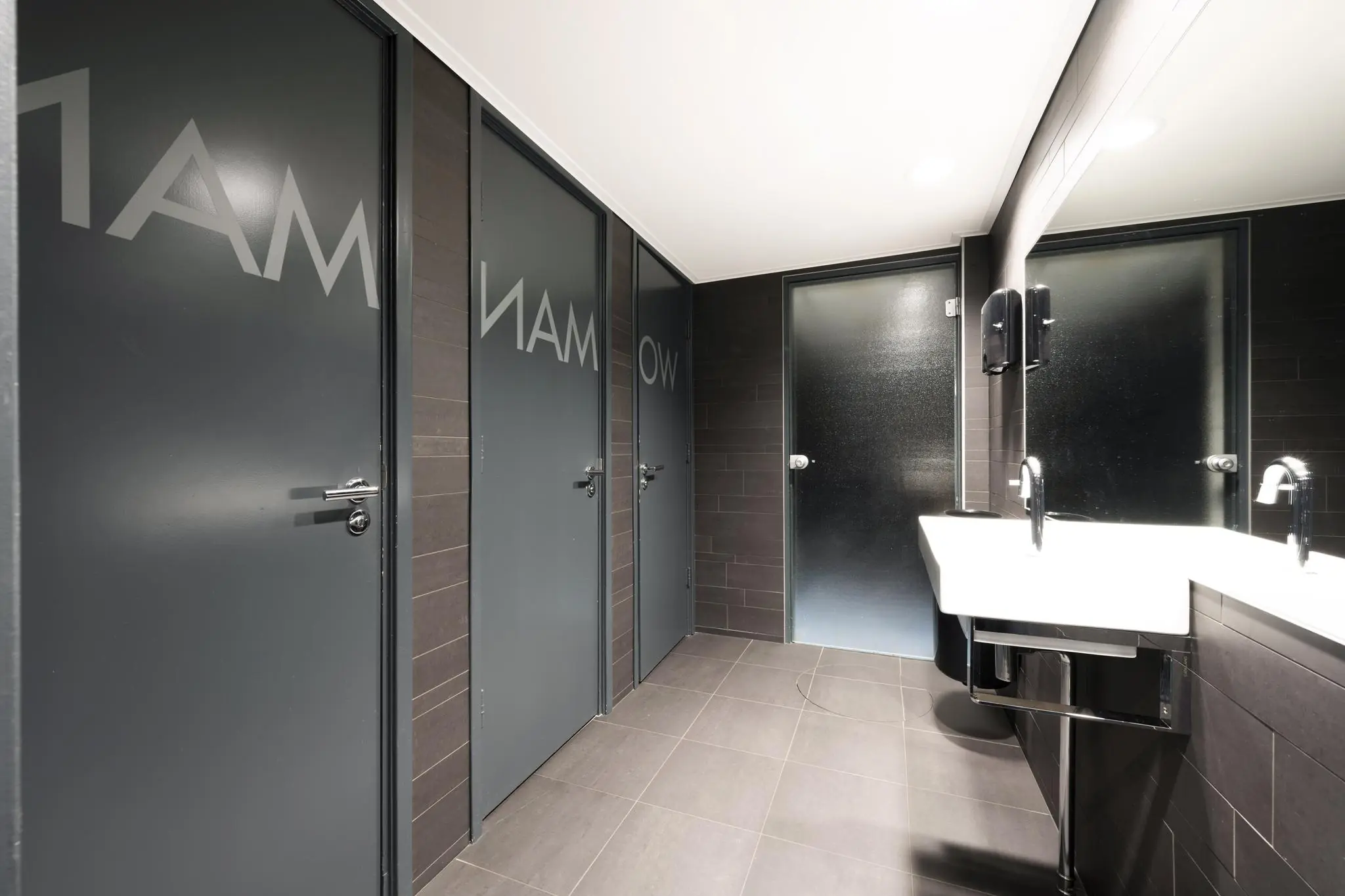 Moderne openbare toiletruimte met grijze deuren, wastafels en spiegel in een gebouw aan de Vliegtuigstraat.