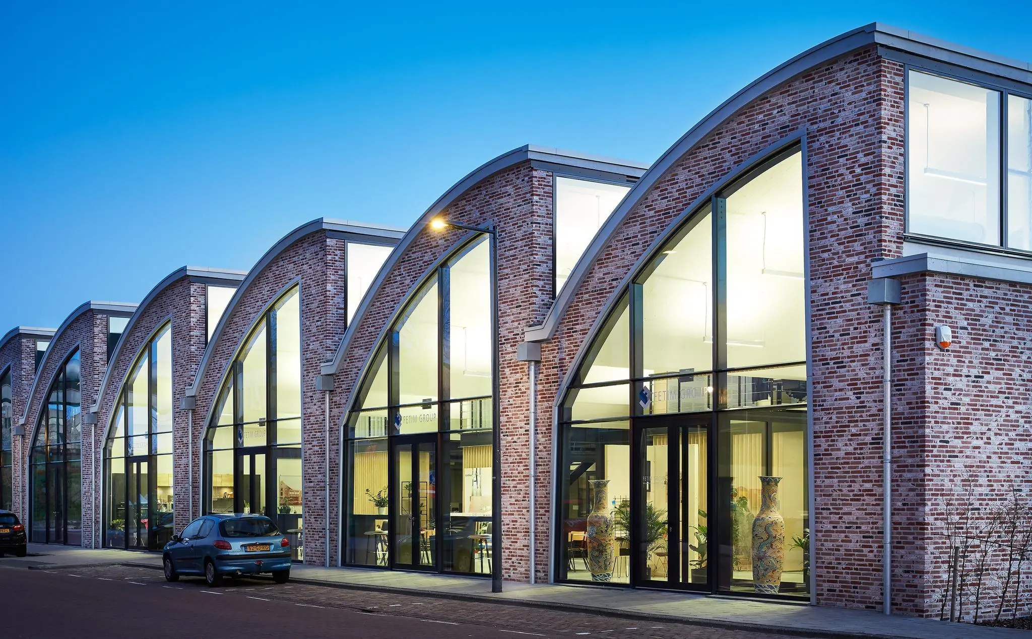 Moderne bakstenen bedrijfsgebouw met grote boogramen aan de Abram Dudok van Heelstraat in de avond.