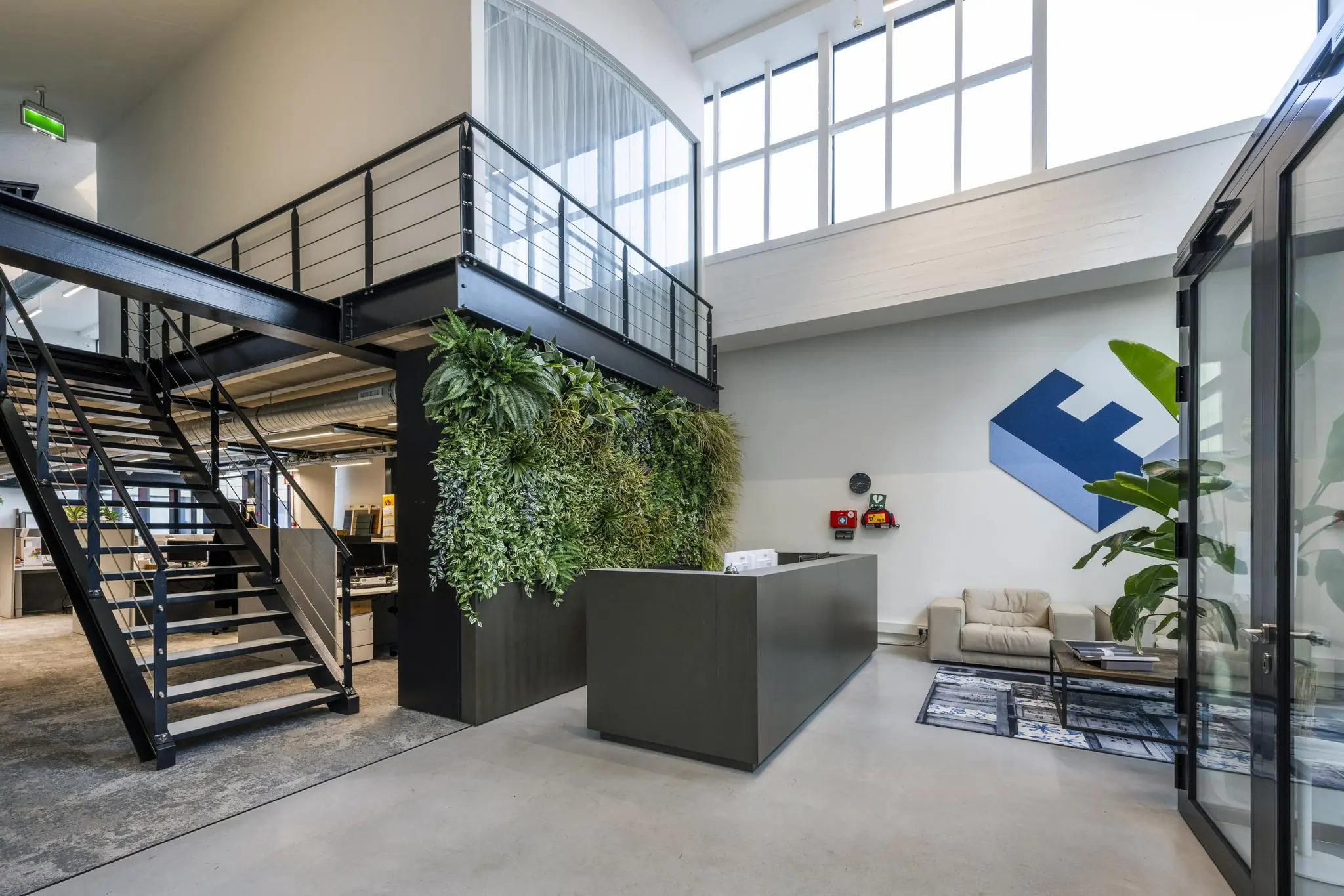 Moderne kantoorentree aan de Abram Dudok van Heelstraat met een groene plantenwand, strakke balie en industriële trap.